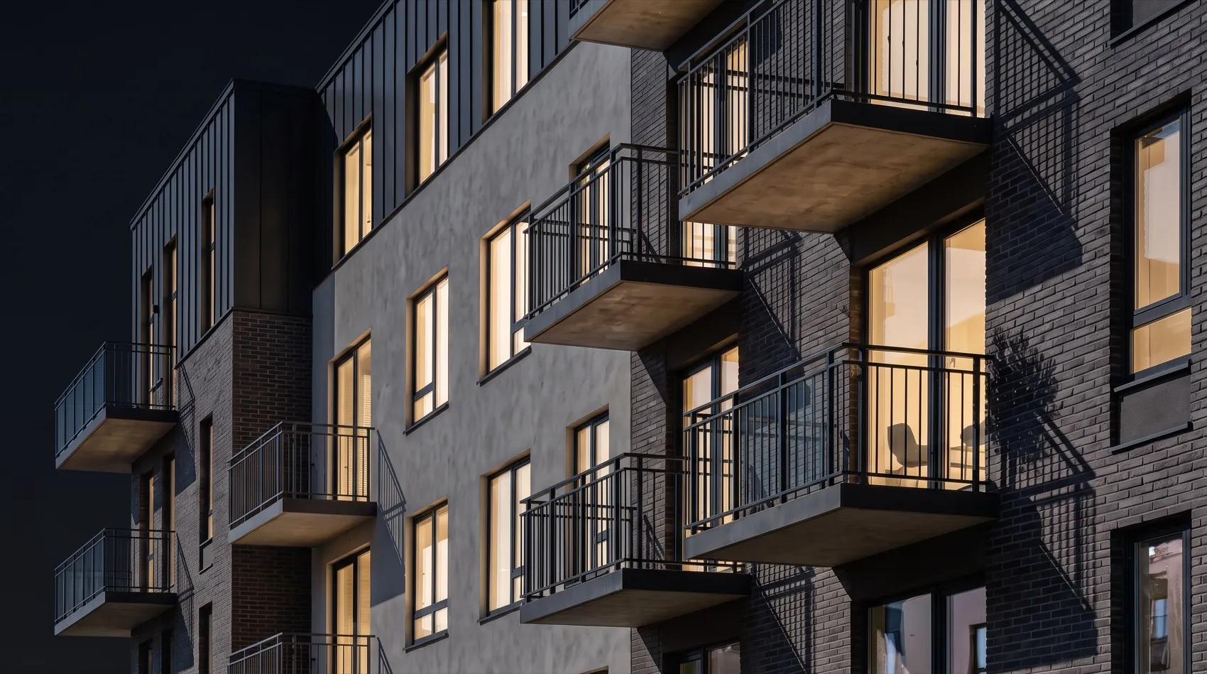 A multifamily building at night, its balconies and lit windows stacked across a dark brick facade.